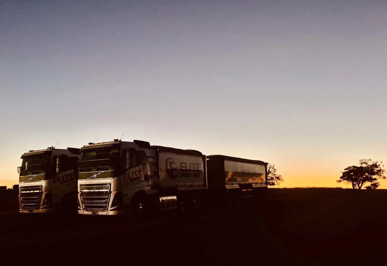Two Elite Haulage Volvo truck-and-dog combinations parked at dusk